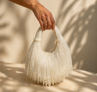 White beaded handbag held by a hand against a neutral background