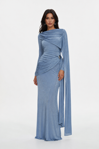 A woman modeling a floor-length light blue draped evening gown with long flowing sleeves and a fitted silhouette, photographed against a clean white studio background.