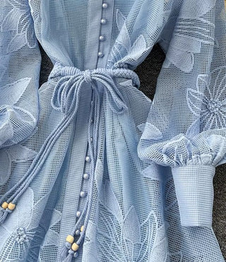 Close-up of a light blue lace dress with floral patterns and buttons.