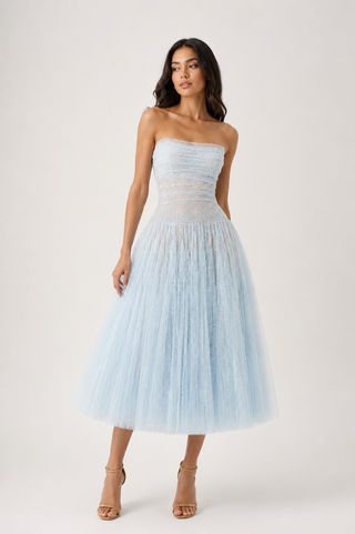 A woman modeling a strapless light blue tulle midi dress with a fitted lace bodice, photographed against a plain light gray studio background.