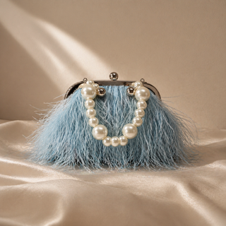 Blue feathered handbag with pearl embellishments on a beige background