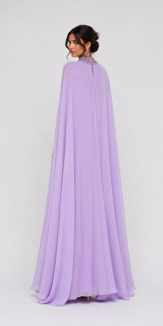 A woman modeling a lavender purple floor-length gown with a high neckline, sheer draped cape sleeves, and a beaded embellished collar, shown from the back against a light gray studio background.