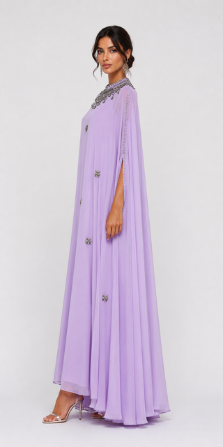 A woman modeling a lavender maxi caftan dress with silver beaded trim at the collar and scattered silver floral embellishments down the front, photographed against a light gray studio background.