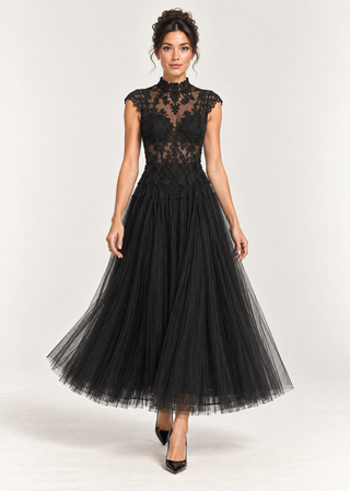 A woman modeling a black lace and tulle formal dress with a high mock neck, cap sleeves, and a full flowing skirt, photographed against a plain light gray studio background.