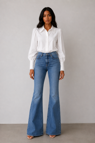 Woman wearing a white blouse and blue flared jeans against a plain background