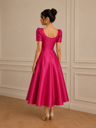 Woman wearing a pink dress with puff sleeves against a beige wall. 1950s style vintage dress elegant midi flared