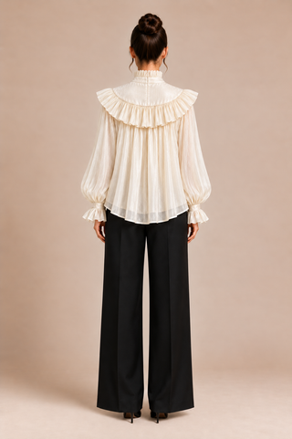 A woman shown from the back wearing a cream ruffled long-sleeve blouse with balloon sleeves and black wide-leg trousers, standing against a plain beige studio background.