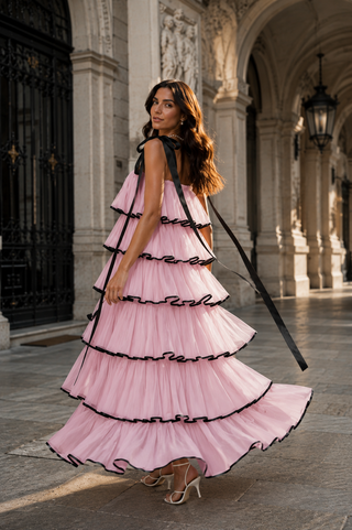 A woman wearing a pink tiered tulle dress with black ribbon trim and a black strap, standing in a stone archway corridor.