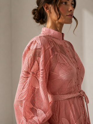 Woman wearing a pink lace dress against a neutral background