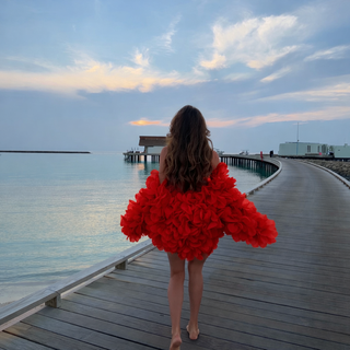 Woman in a red dress standing on a wooden pier overlooking the water at sunset.