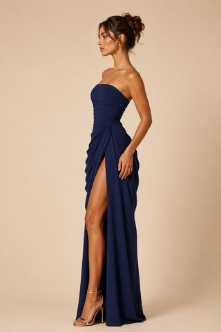 Woman wearing a strapless navy blue gown with a high slit on a beige background