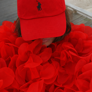 Person wearing a red cap with a logo, surrounded by red fabric.