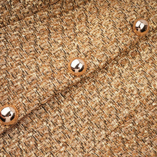 Close-up of a textured tweed fabric in warm beige, brown, and gold tones, with three shiny metallic buttons arranged diagonally.