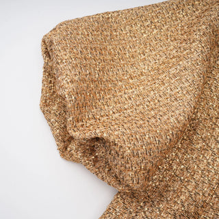 A close-up of draped tweed fabric in a warm tan and brown colorway, showing the woven texture against a plain white background.