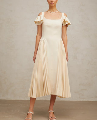 Woman wearing a neutral pleated midi dress with flutter sleeves and darted bodice, ideal for elegant summer events, wedding guest looks, or garden parties.