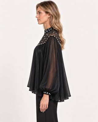 A woman shown in side profile wearing a black sheer long-sleeve blouse with a high neckline and silver rhinestone embellishments, paired with black pants, against a plain light background.