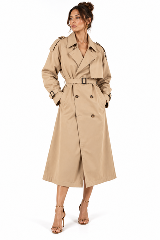 A woman modeling a classic double-breasted trench coat in beige. The coat features a matching waist belt with a silver buckle, epaulets, and a double-breasted button closure.