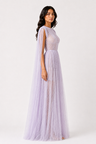 A woman modeling a lavender purple tulle maxi dress with a sheer lace bodice, cap sleeves, and a flowing tulle skirt, photographed against a plain white studio background.