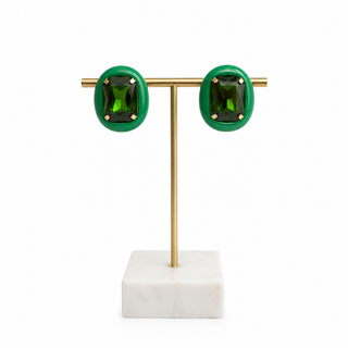 A pair of oval green stud earrings with rectangular green center stones and gold-toned settings, displayed on a gold T-stand with a white marble base against a white background.