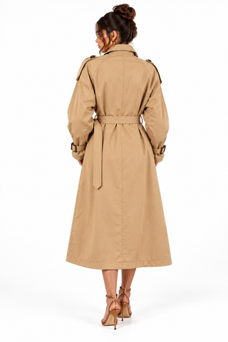 A woman viewed from behind wearing a classic tan trench coat with a matching waist tie, paired with tan high-heeled sandals, against a plain white studio background.