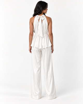 A woman viewed from the back wearing a white satin halter top with a tie-back detail and matching wide-leg pants against a plain white studio background.