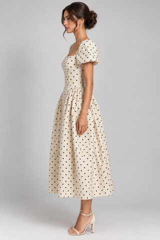 A woman modeling a cream midi dress with black polka dots, featuring short puff sleeves and a square neckline, shown from a side profile against a light gray studio background.