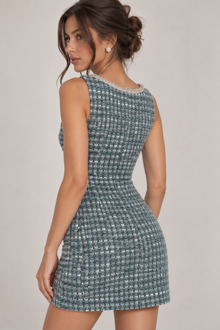 A woman modeling a sleeveless, bodycon mini dress made of a textured tweed-like fabric in blue, gray, and white, shown from a three-quarter back angle against a plain light gray studio background.