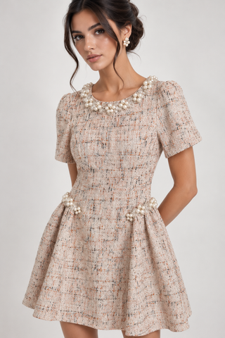 A woman modeling a short-sleeve tweed fit-and-flare dress in a beige and brown woven pattern, featuring a pearl-beaded collar and matching pearl bead details at the waist, set against a plain light gray studio background.