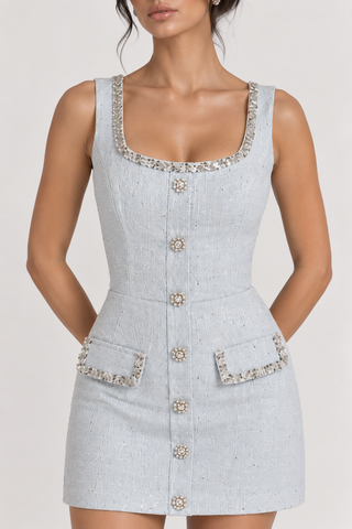 A sleeveless light gray tweed mini dress with a square neckline, decorative crystal-embellished trim, a front button closure, and two front patch pockets, shown on a model against a plain light background.