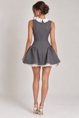 A woman shown from the back wearing a sleeveless gray mini dress with a white patterned Peter Pan collar and a flared skirt, paired with white high heels, against a light gray studio background.