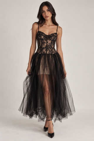 A woman models a black lace and tulle formal dress with spaghetti straps, a structured lace bodice, and a voluminous sheer tulle skirt against a plain light gray studio background.