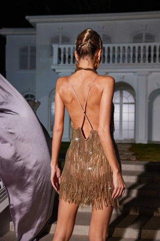 Woman in a gold fringe dress standing in front of a white building at night.