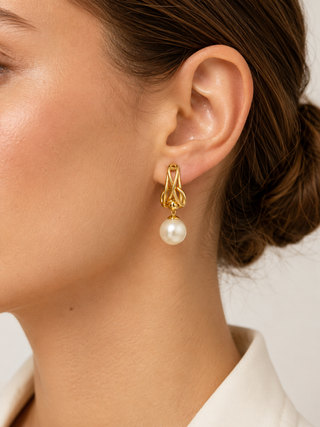 A close-up of a model's ear wearing a gold drop earring with an intricate gold top and a dangling white pearl.