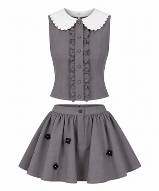 A two-piece girls' outfit set in gray, featuring a sleeveless vest with a white scalloped Peter Pan collar and ruffle trim, paired with a matching flared skirt adorned with black flower appliqués.