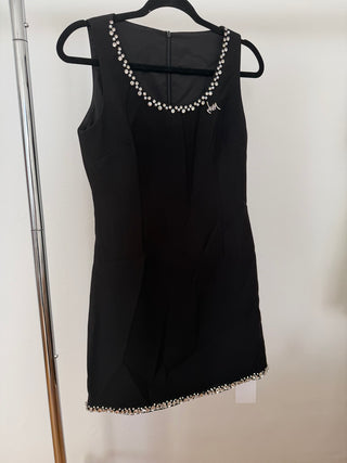 A sleeveless black dress with a scoop neckline and a matching beaded border, hanging on a black hanger against a plain light background.