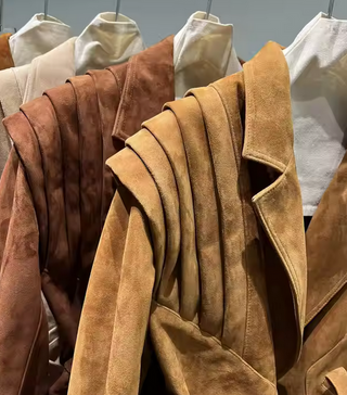 Premium wild leather goatskin suede jackets with pleated shoulder detailing, available in tan, rust brown, beige, and black, hanging on a clothing rack with adjustable belted waists for a tailored fit. Drejani Leather Jacket Suede, Wildleather Jacket Real Leather