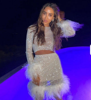 Person wearing a sparkling outfit with feather details on a reflective surface at night.