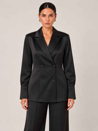 A woman modeling a black double-breasted blazer with matching trousers, photographed against a plain light gray studio background.