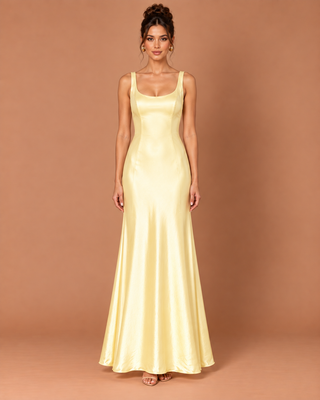 A woman modeling a floor-length satin slip dress in pale yellow against a solid warm tan studio backdrop.