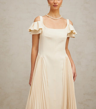 Woman wearing a neutral pleated midi dress with flutter sleeves and darted bodice, ideal for elegant summer events, wedding guest looks, or garden parties.