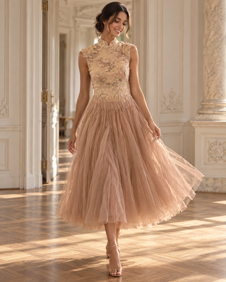 A woman wearing a sleeveless champagne lace bodice and a voluminous blush pink tulle midi skirt, standing in a sunlit classical hallway.