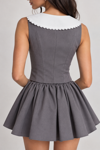 A woman shown from the back wearing a sleeveless gray dress with a large white scalloped Peter Pan collar and a flared skirt, against a light gray studio background.