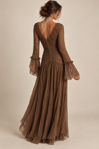 A woman modeling a brown long-sleeve maxi dress from the back, featuring a ruched back, sheer bell sleeves, and a flowing pleated skirt against a neutral beige background.