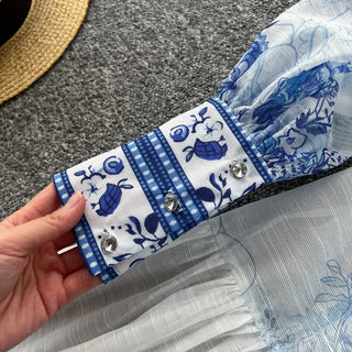 Hand holding a blue and white patterned fabric with decorative elements on a gray surface.