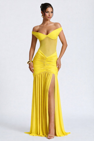 Woman wearing a yellow off-shoulder evening gown with a slit on a white background