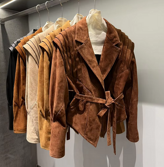 Premium wild leather goatskin suede jackets with pleated shoulder detailing, available in tan, rust brown, beige, and black, hanging on a clothing rack with adjustable belted waists for a tailored fit. Drejani Leather Jacket Suede, Wildleather Jacket