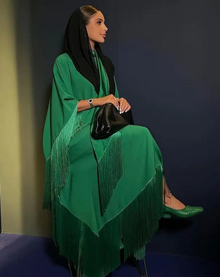 Woman in a green dress with fringe sitting against a dark background