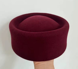 Maroon felt hat held by a hand against a white background