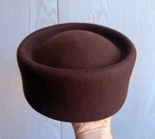 Brown felt hat held against a light wooden panel background