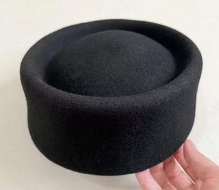 Black felt hat held by a hand on a light background
